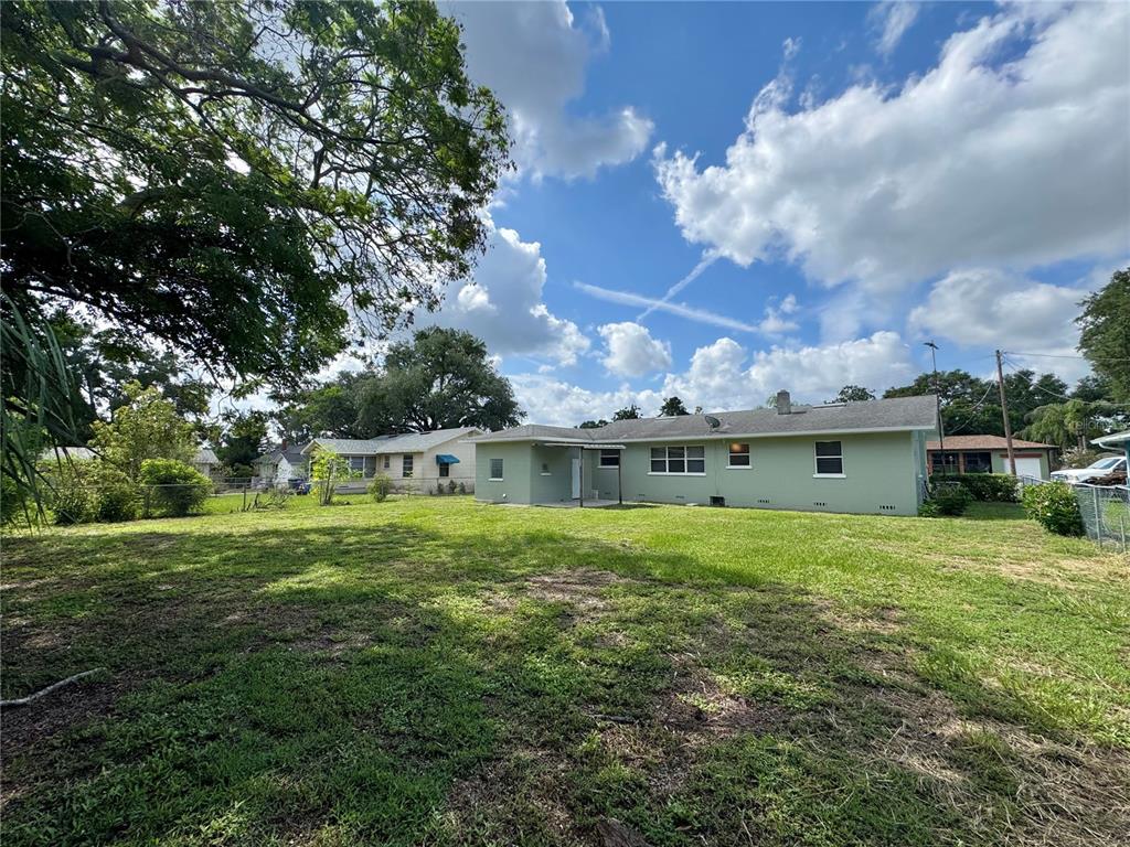 The backyard of a light green single-story house features a large lawn and trees — 921 AVENUE E NE, WINTER HAVEN, FL