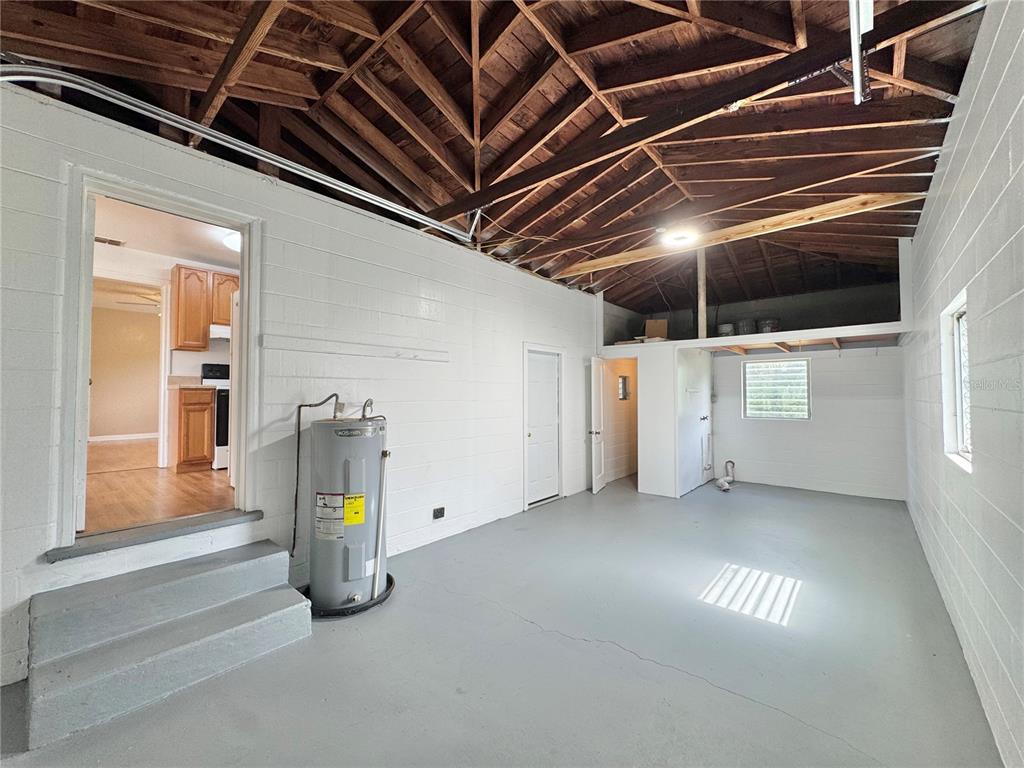 A garage with a water heater, exposed wooden rafters, and a doorway leading to a kitchen — 921 AVENUE E NE, WINTER HAVEN, FL