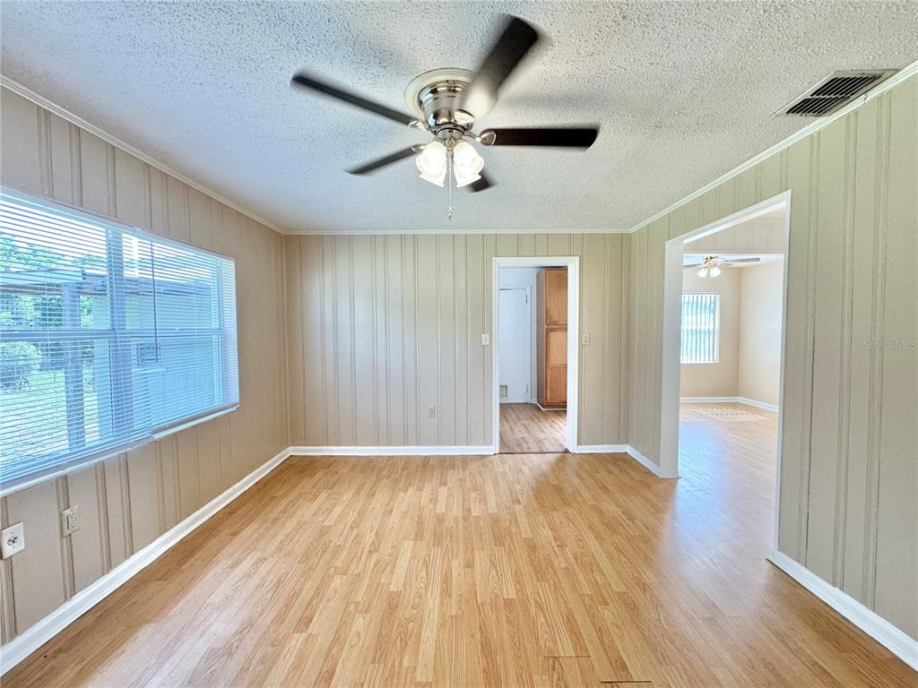 A room with wood-look flooring, paneled walls, a ceiling fan, and views into adjacent rooms — 921 AVENUE E NE, WINTER HAVEN, FL