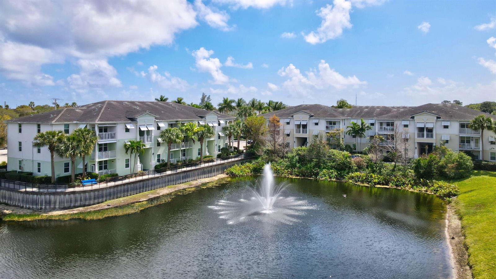 An aerial view shows two apartment buildings overlooking a pond with a central water fountain — 3615 High Ridge Road # 201, Boynton Beach FL 33426, BOYNTON BEACH, FL
