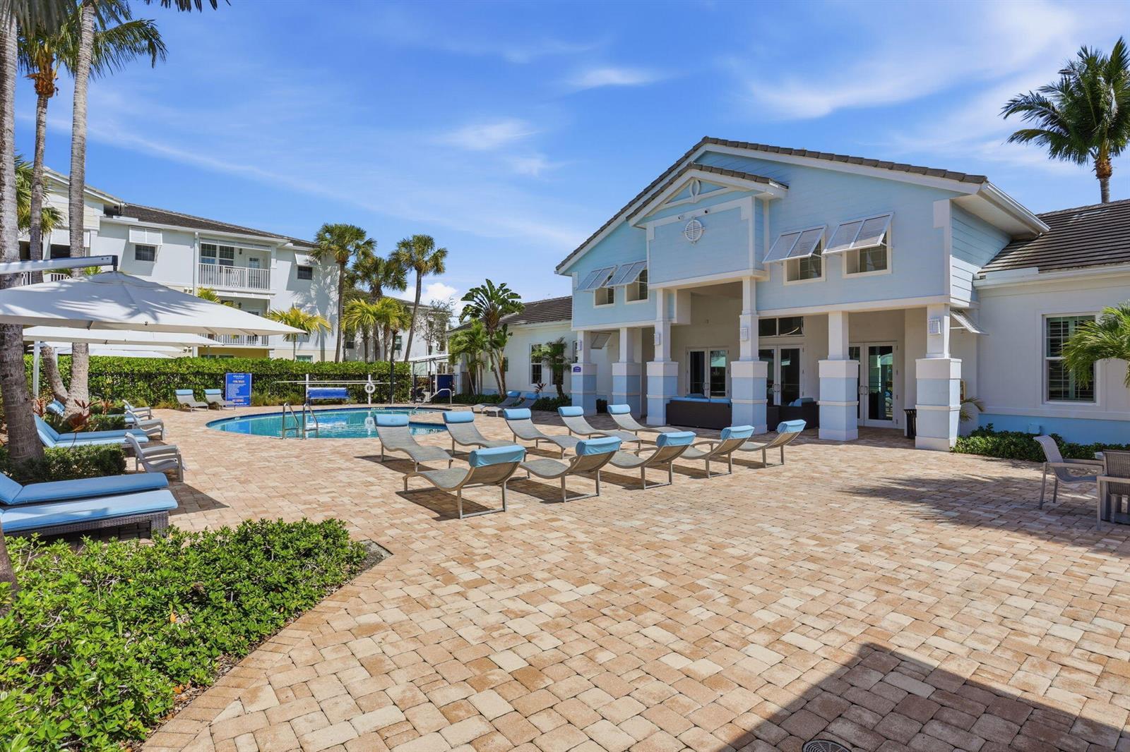 A swimming pool area with lounge chairs on a brick patio beside a light blue building — 3615 High Ridge Road # 201, Boynton Beach FL 33426, BOYNTON BEACH, FL