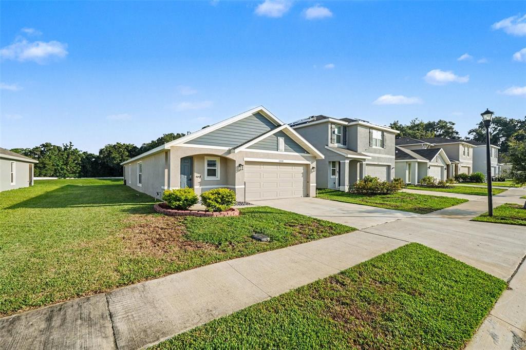 A single-story suburban house with a tan stucco exterior, gray siding, and a two-car garage — 13530 MOUNT IVY COURT, DADE CITY, FL