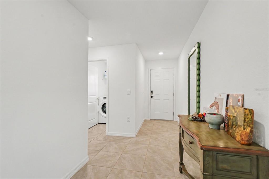 A tiled entryway features a wooden console table, a wall mirror, and a laundry room door — 13530 MOUNT IVY COURT, DADE CITY, FL