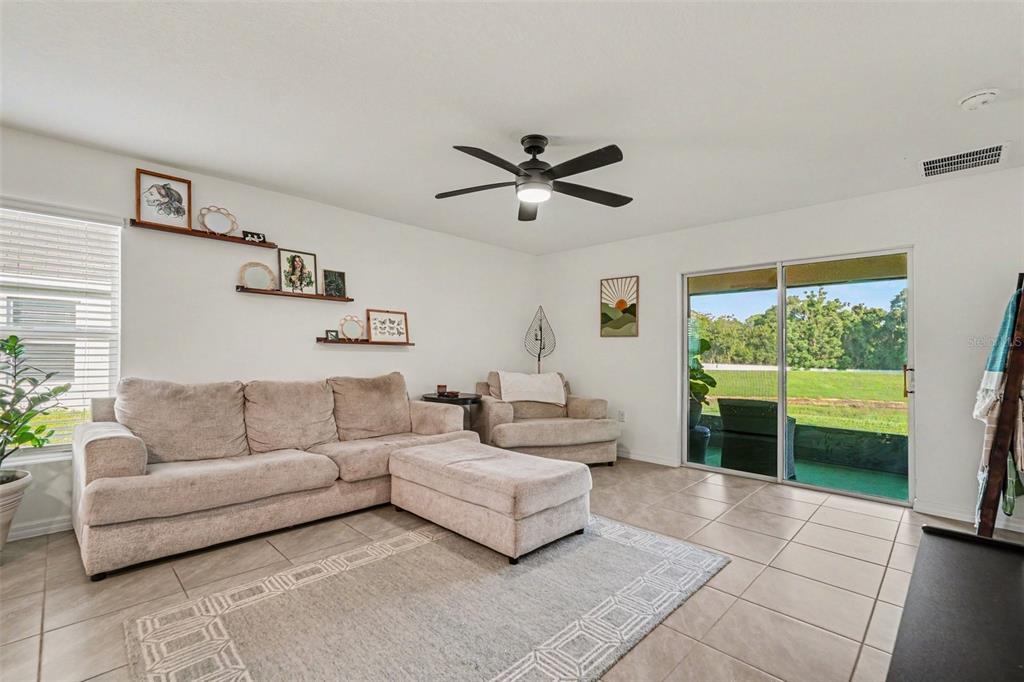 A living room with a beige sectional sofa, tile flooring, and a sliding glass door — 13530 MOUNT IVY COURT, DADE CITY, FL