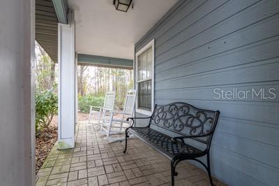 A covered porch features a brick floor, blue siding, a metal bench, and two rocking chairs — 6658 NW 36TH TERRACE, GAINESVILLE, FL