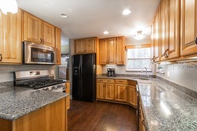 A kitchen features light wood cabinets, granite countertops, stainless steel appliances, and dark wood flooring — 6658 NW 36TH TERRACE, GAINESVILLE, FL