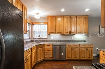 A kitchen features light wood cabinets, granite countertops, stainless steel appliances, and dark wood flooring — 6658 NW 36TH TERRACE, GAINESVILLE, FL