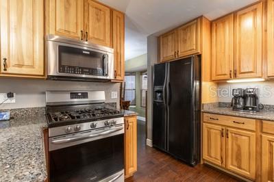 A kitchen features light wood cabinets, granite countertops, stainless steel appliances, and a black refrigerator — 6658 NW 36TH TERRACE, GAINESVILLE, FL