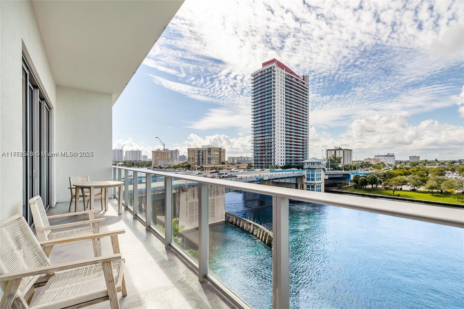A balcony with chairs and a table overlooks a river, a bridge, and city buildings — 4010 S Ocean Dr # R406, Hollywood FL 33019, HOLLYWOOD, FL