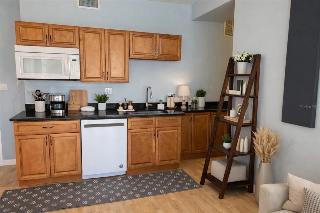 A kitchen features wooden cabinets, black countertops, a white dishwasher, and a wooden ladder shelf — 101 PALM HARBOR PARKWAY UNIT OC2, PALM COAST, FL