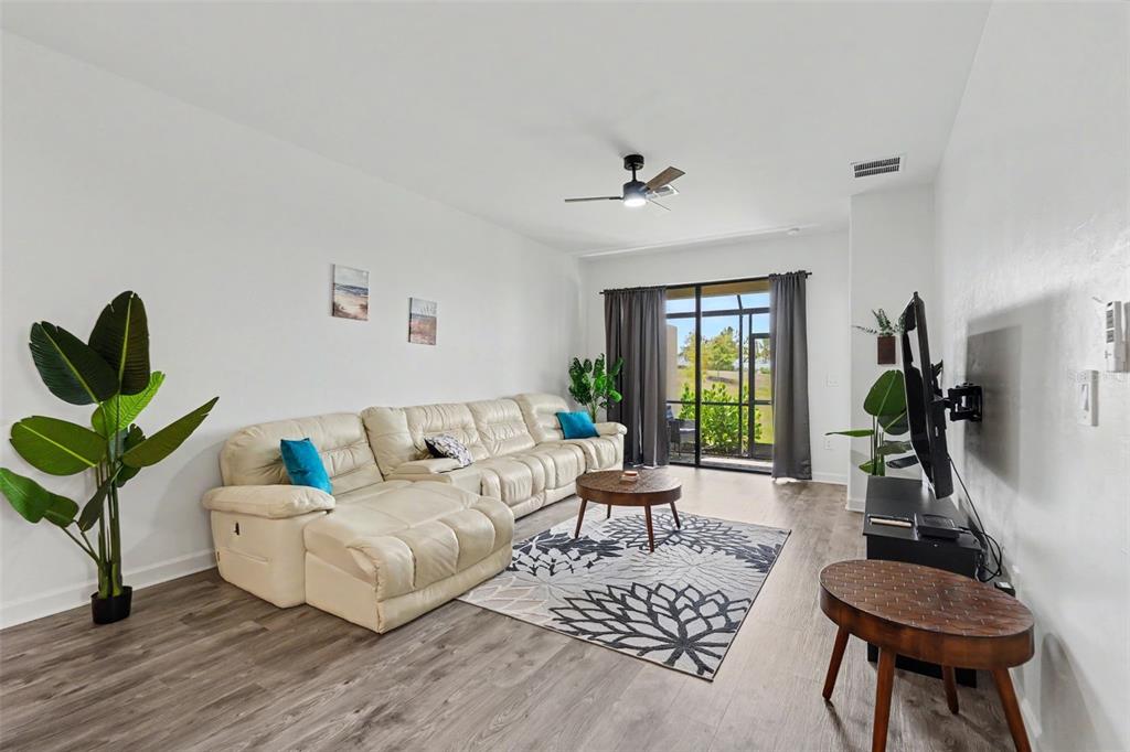 A living room features a cream sectional sofa, a patterned area rug, and sliding glass doors — 15724 SUNNY DAY DRIVE, BRADENTON, FL
