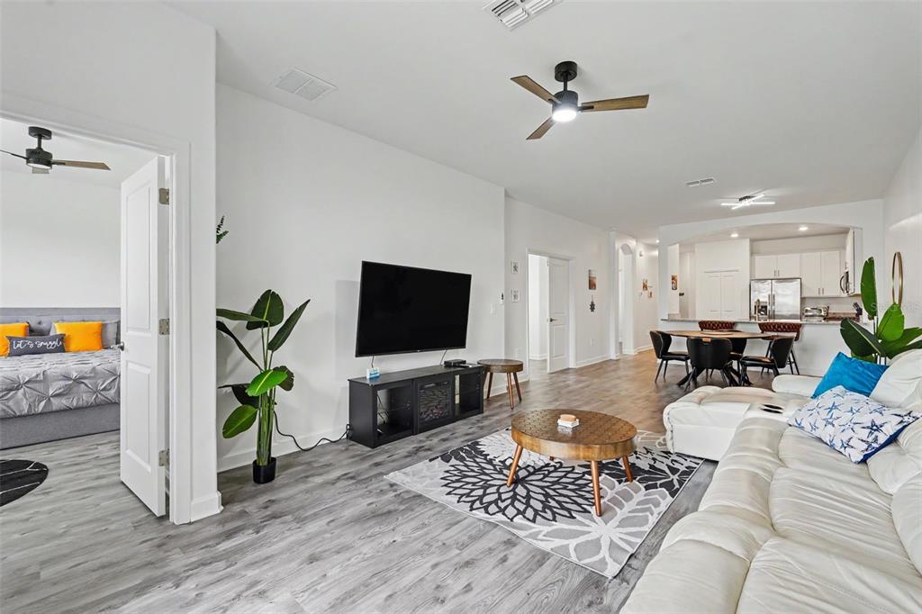 A living room with wood-look flooring, a wall-mounted television, and an open-concept kitchen — 15724 SUNNY DAY DRIVE, BRADENTON, FL