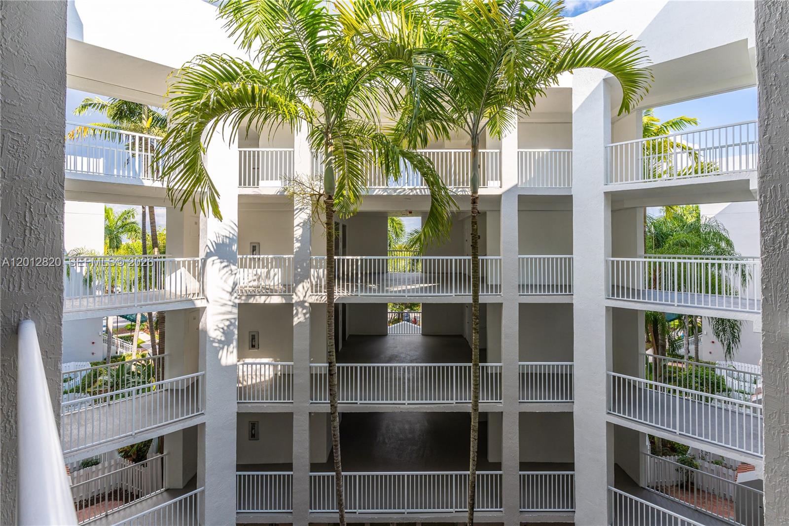An open-air apartment building courtyard features white railings, concrete walkways, and two tall palm trees — 10750 NW 66th St # 408, Doral FL 33178, DORAL, FL
