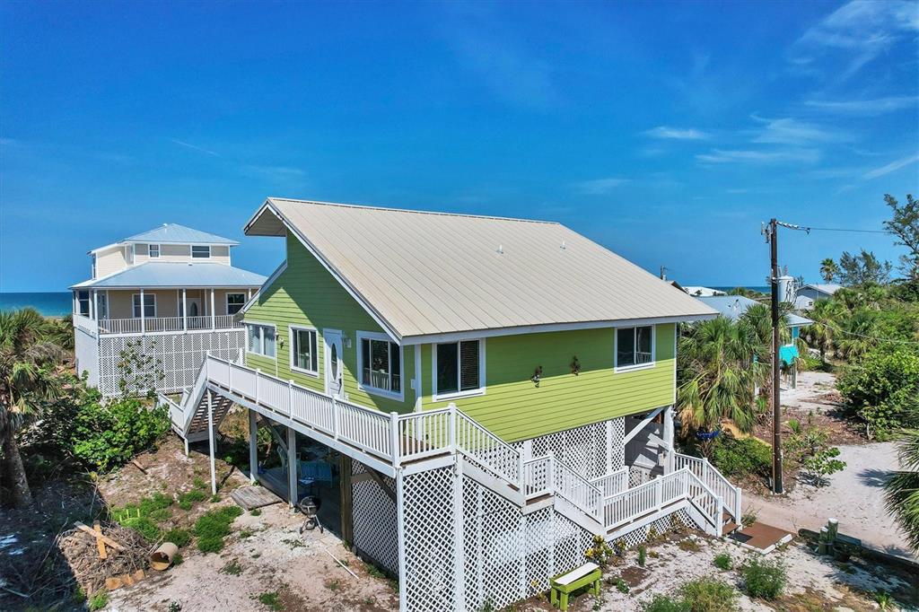 An elevated, light green house with a metal roof stands near the beach — 9350 LITTLE GASPARILLA ISLAND, PLACIDA, FL