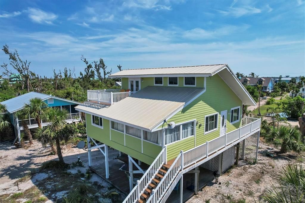 An elevated, light green coastal house with a metal roof and a wooden staircase — 9350 LITTLE GASPARILLA ISLAND, PLACIDA, FL