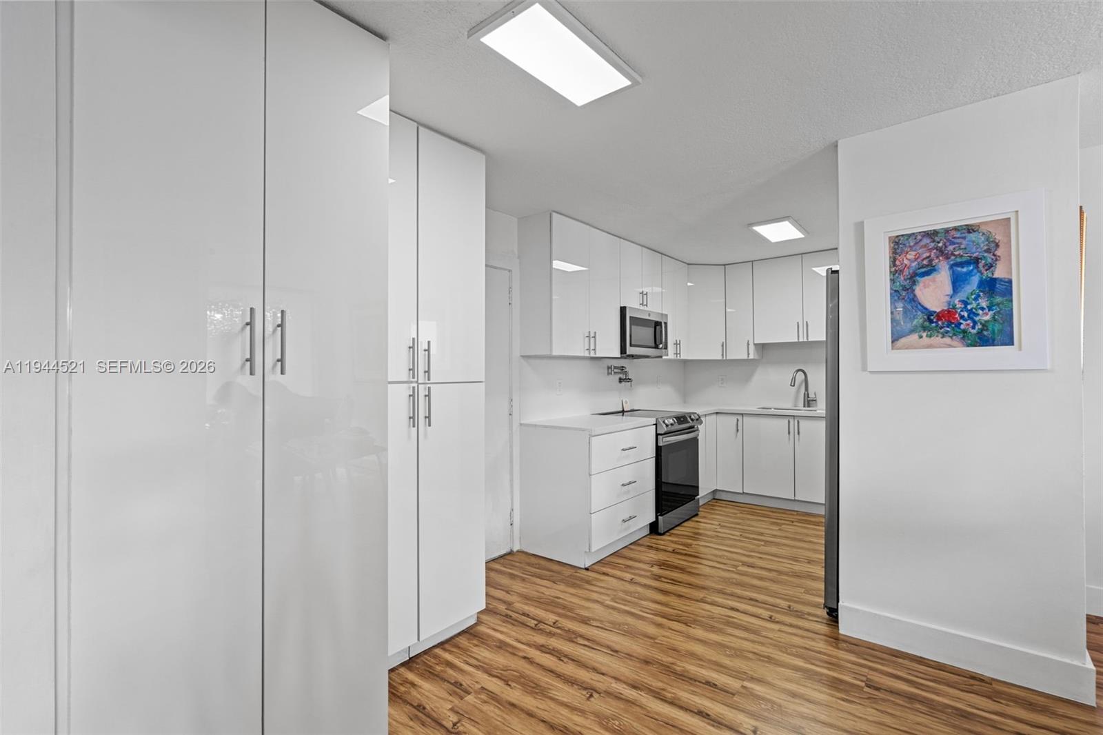A modern kitchen features white glossy cabinets, stainless steel appliances, and wood-look flooring — 13953 Kendale Lakes Cir # 608B, Miami FL 33183, MIAMI, FL