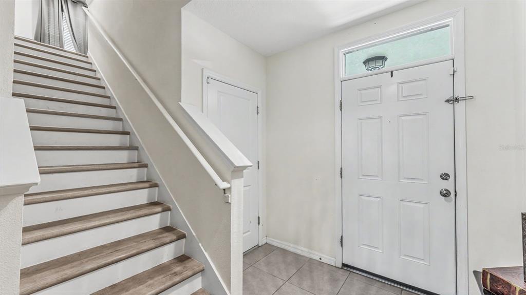 A foyer features a staircase with wood-look treads, a white front door, and tiled flooring — 3509 DIAMOND LEAF COURT, VALRICO, FL