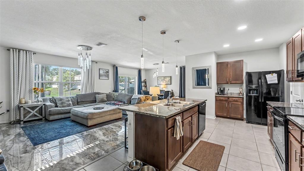 An open-concept kitchen with dark wood cabinets and a granite island overlooks a living area — 3509 DIAMOND LEAF COURT, VALRICO, FL
