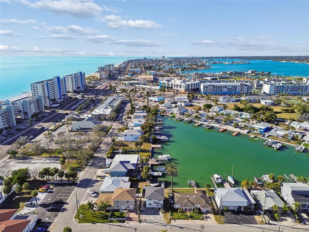 An aerial view shows a coastal town with high-rise buildings, residential homes, and a canal — 14919 N BAYSHORE DRIVE UNIT 1, MADEIRA BEACH, FL