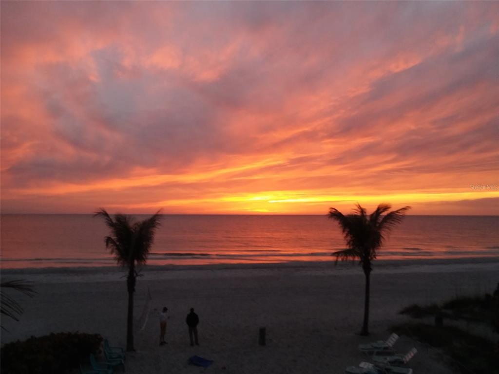 A beach view at sunset with two palm trees and two people on the sand — 14919 N BAYSHORE DRIVE UNIT 1, MADEIRA BEACH, FL