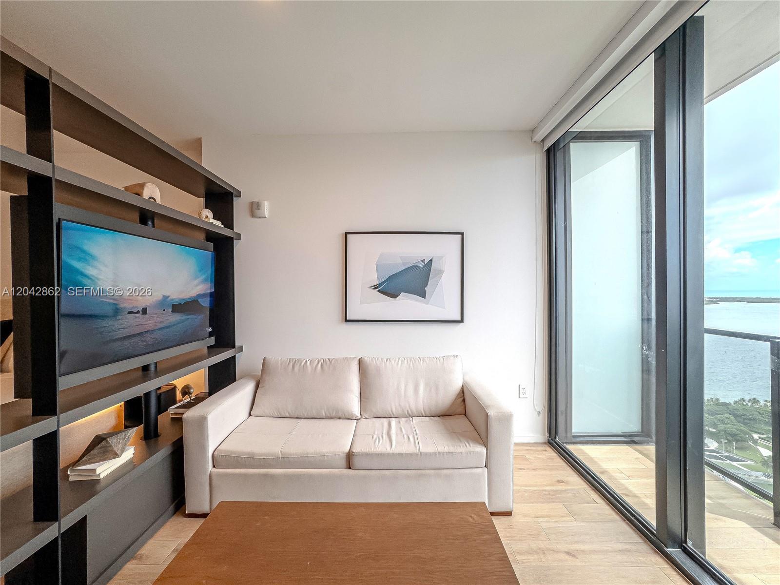 A living room features a beige sofa, a dark shelving unit with a television, and a balcony — 398 NE 5th St # 4316, Miami FL 33132, MIAMI, FL
