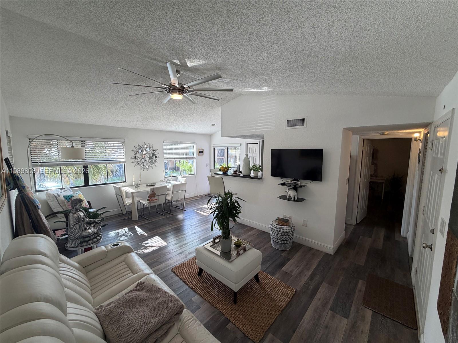 A living room features white walls, dark wood-look flooring, a ceiling fan, and dining area — 10670 SW 156th Pl # 308, Miami FL 33196, MIAMI, FL
