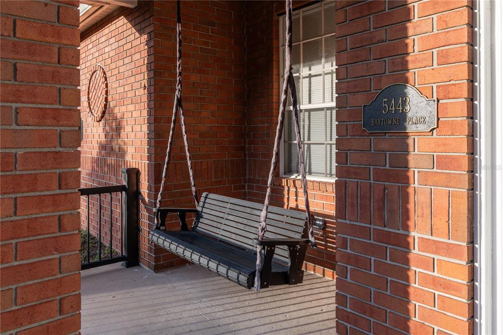 A black porch swing hangs on a brick patio next to a window — 5443 BAYTOWNE PLACE, OVIEDO, FL