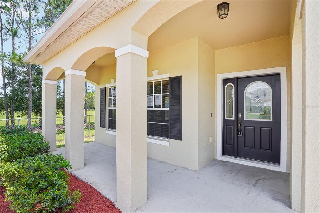 A covered front porch with beige stucco walls, white columns, and a dark front door — 2331 CARNATION HILL COURT, ORLANDO, FL