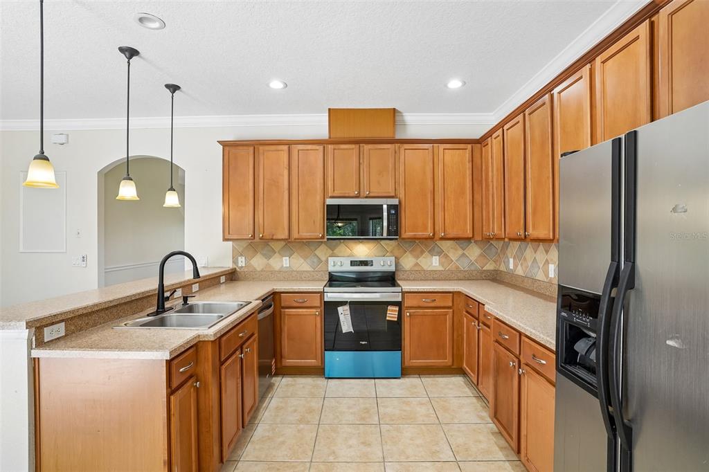 A kitchen features wood cabinets, stainless steel appliances, tile backsplash, and a double basin sink — 2331 CARNATION HILL COURT, ORLANDO, FL