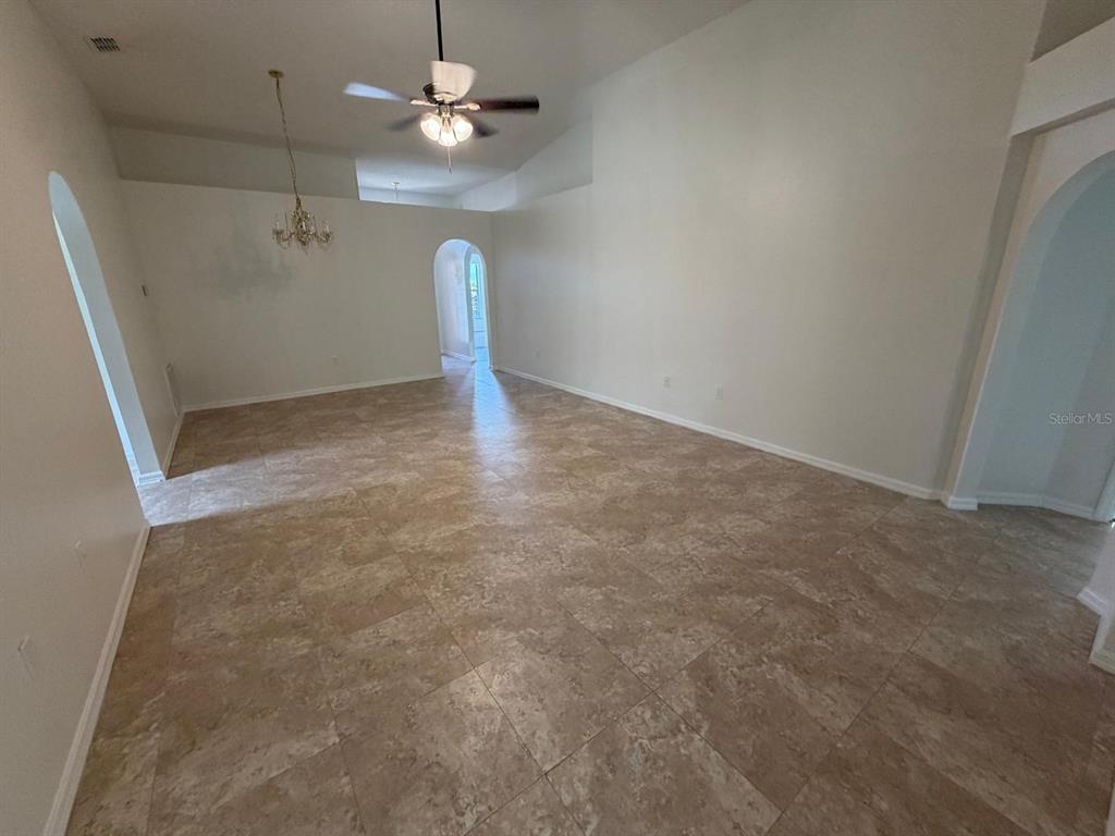 An empty room features light-colored tile flooring, white walls, a ceiling fan, and arched doorways — 3015 ELBIB DRIVE, ST CLOUD, FL