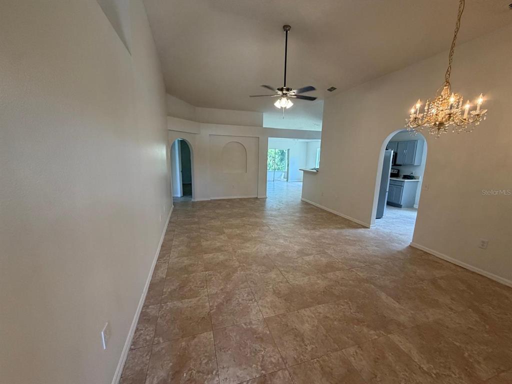 A large, open-concept room with tan tile flooring, a ceiling fan, and a crystal chandelier — 3015 ELBIB DRIVE, ST CLOUD, FL
