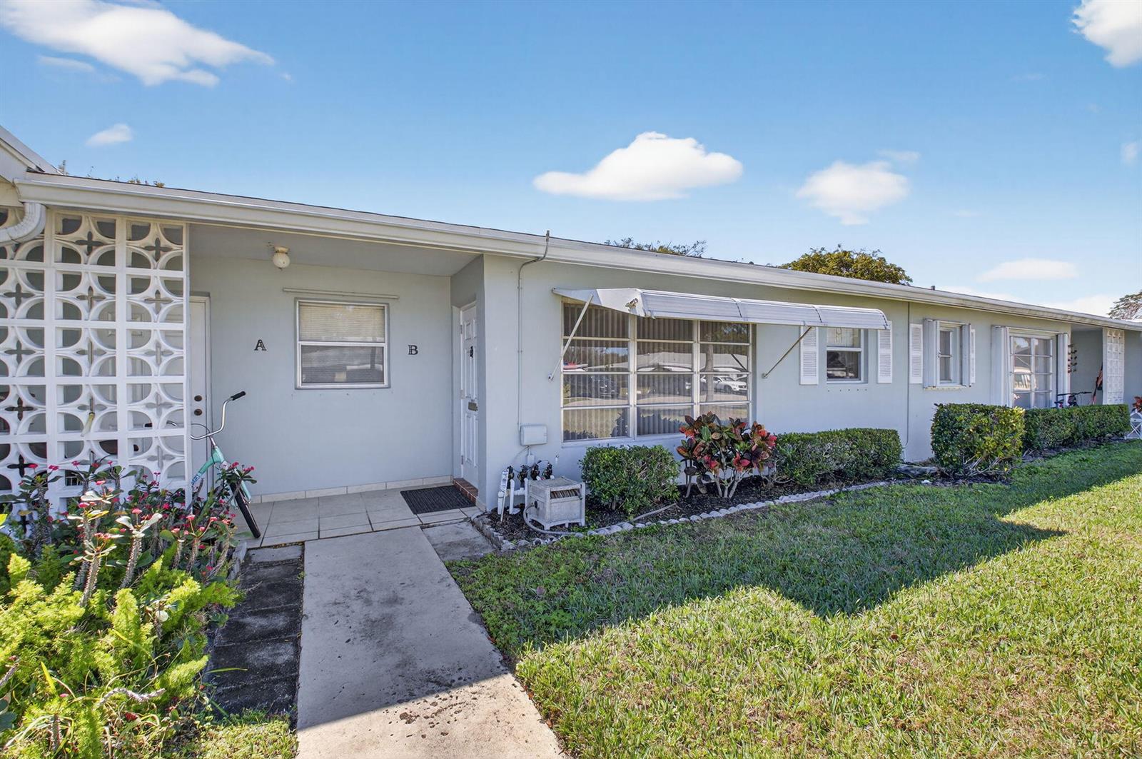 A single-story residential building with light-colored walls, a concrete walkway, and decorative breeze block accents — 220 High Point Court E # B, Delray Beach FL 33445, DELRAY BEACH, FL