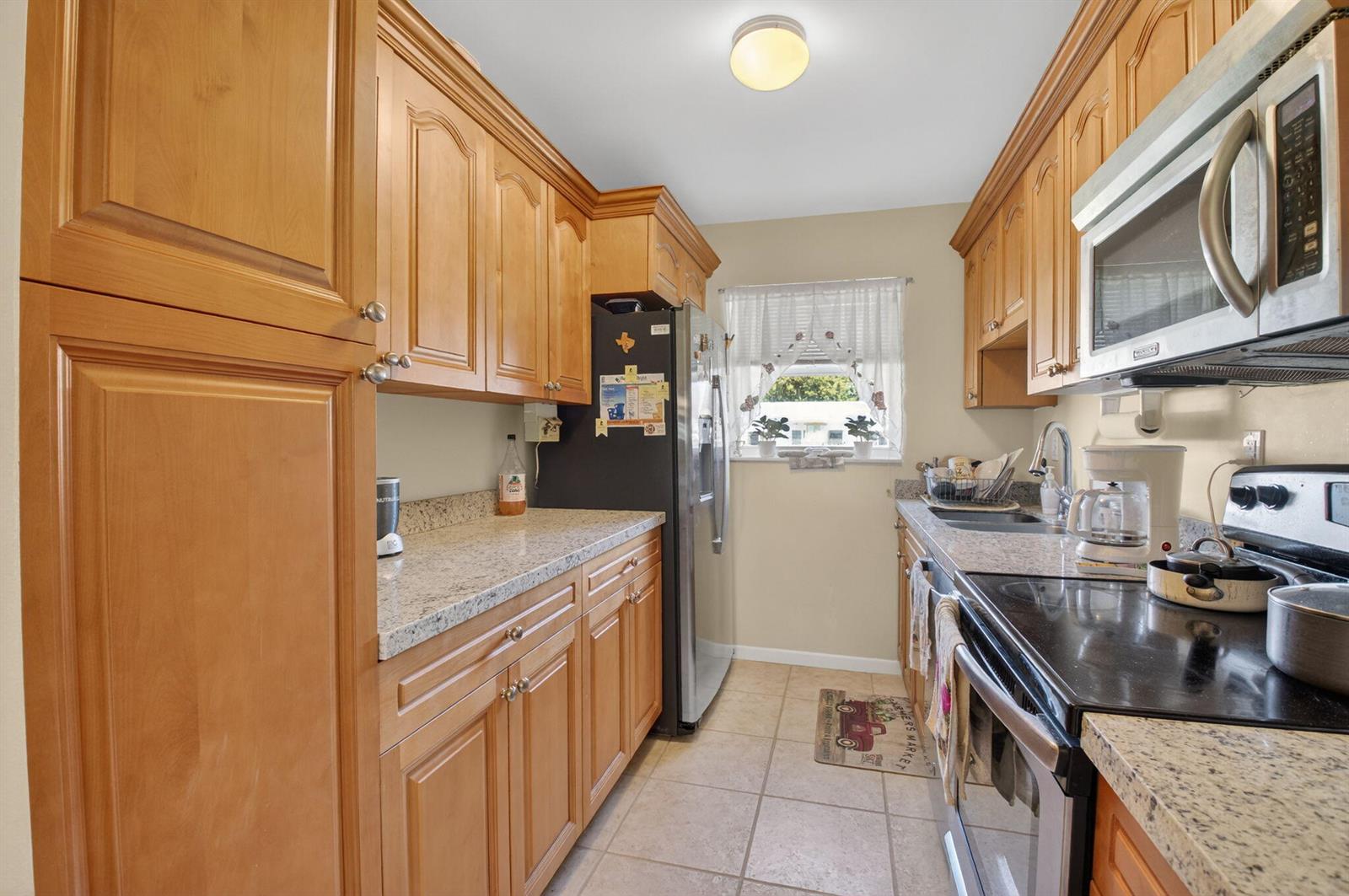 A galley kitchen features light wood cabinets, granite countertops, stainless steel appliances, and tile flooring — 220 High Point Court E # B, Delray Beach FL 33445, DELRAY BEACH, FL