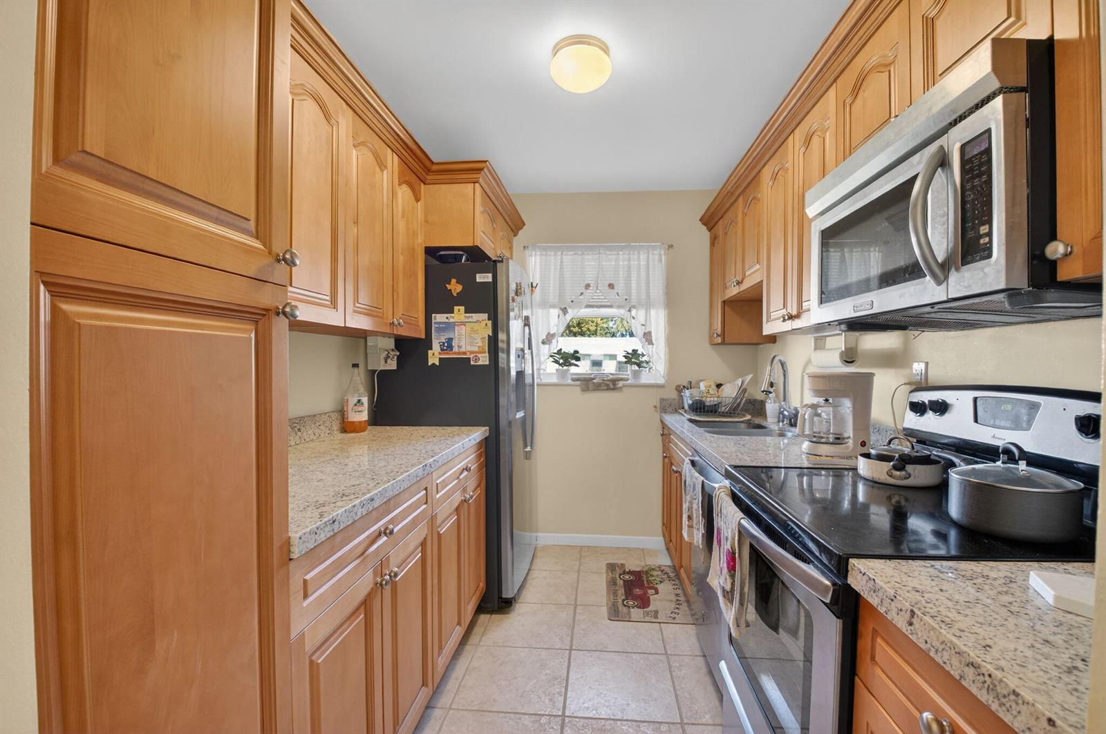 A galley kitchen features light wood cabinets, granite countertops, and stainless steel appliances — 220 High Point Court E # B, Delray Beach FL 33445, DELRAY BEACH, FL