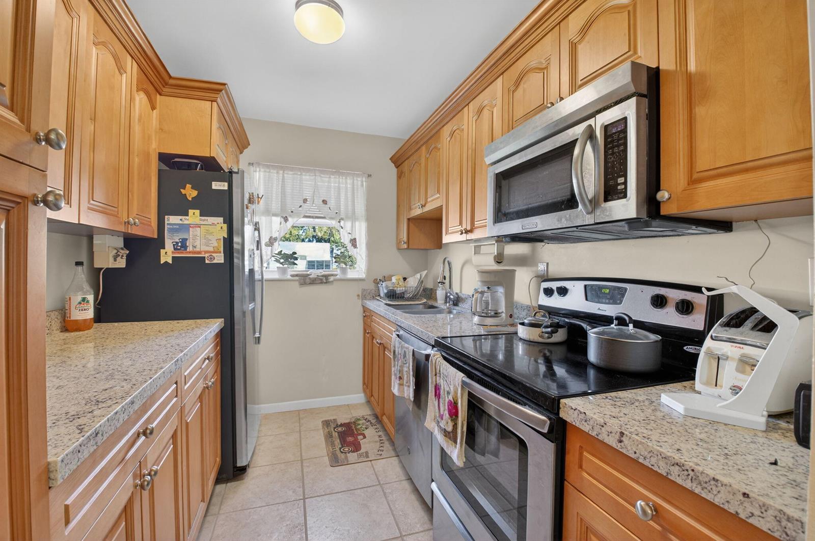 A galley kitchen features light wood cabinets, granite countertops, and stainless steel appliances — 220 High Point Court E # B, Delray Beach FL 33445, DELRAY BEACH, FL
