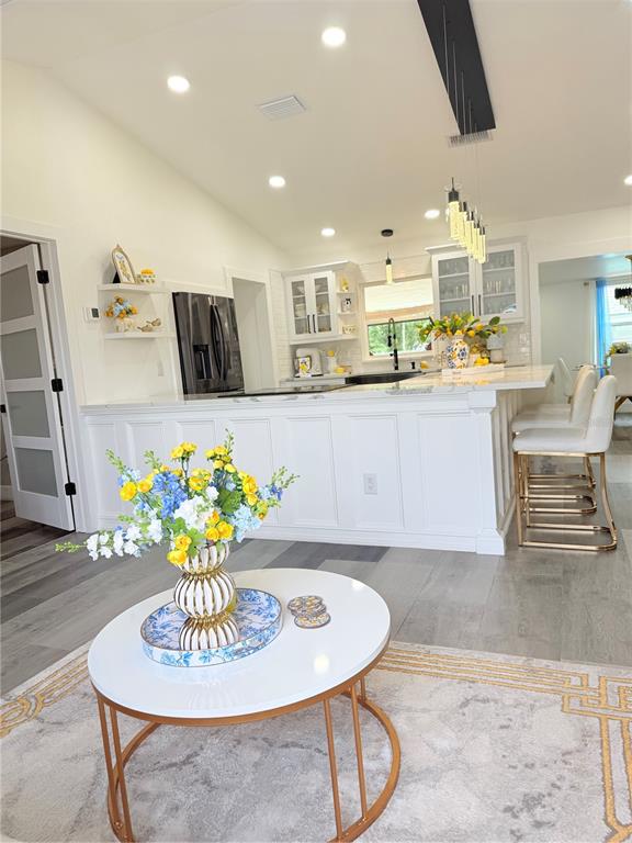 A bright kitchen features white cabinetry, a large island with bar seating, and wood flooring — 608 JAGUAR COURT, POINCIANA, FL
