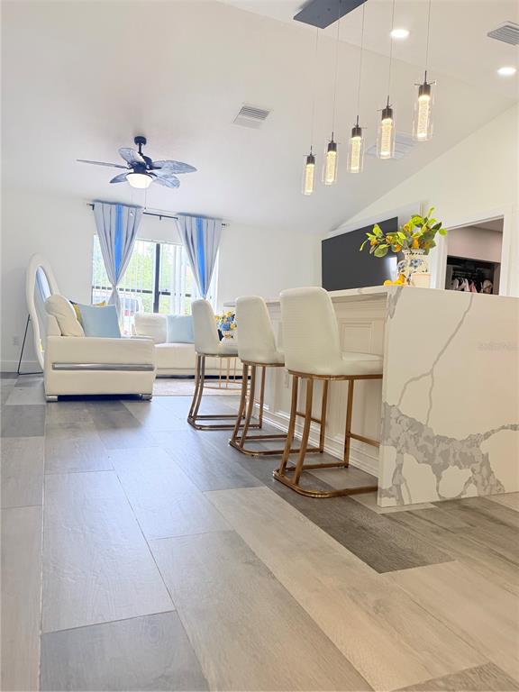 A kitchen island with bar stools sits in an open-concept living area with wood-look flooring — 608 JAGUAR COURT, POINCIANA, FL