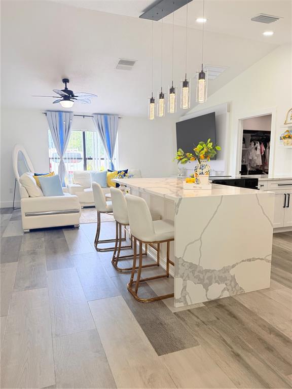 A kitchen island with a marble-look countertop and bar stools sits before a living area — 608 JAGUAR COURT, POINCIANA, FL