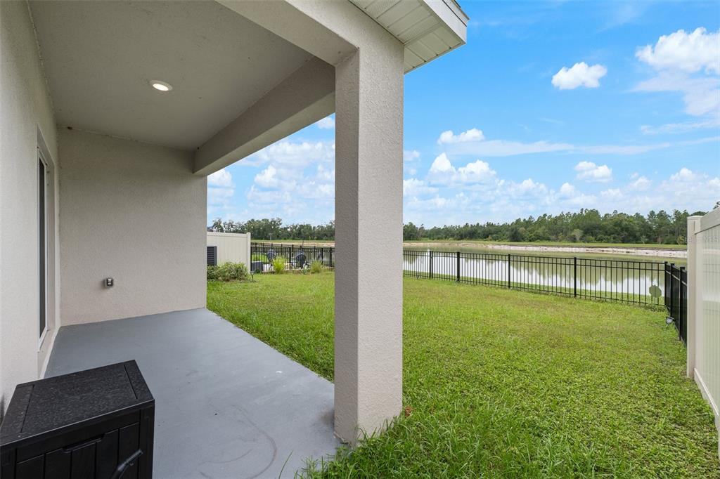 A covered concrete patio overlooks a grassy backyard with a black fence and a pond — 35630 KINSEY POINT, ZEPHYRHILLS, FL