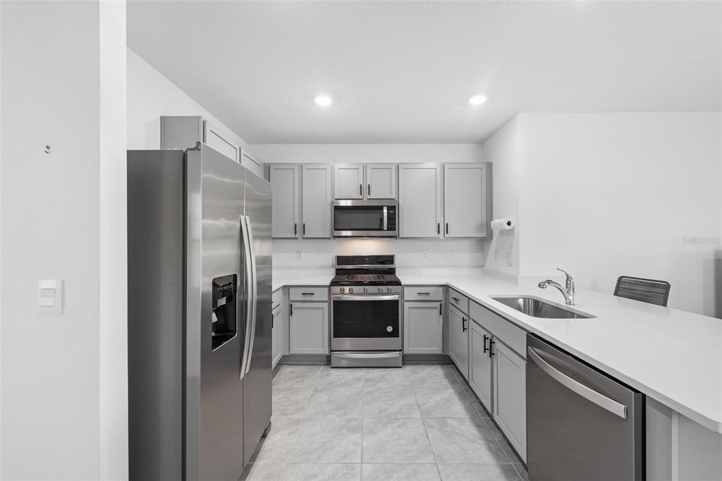 A modern kitchen features gray cabinets, stainless steel appliances, and a white countertop island — 35630 KINSEY POINT, ZEPHYRHILLS, FL