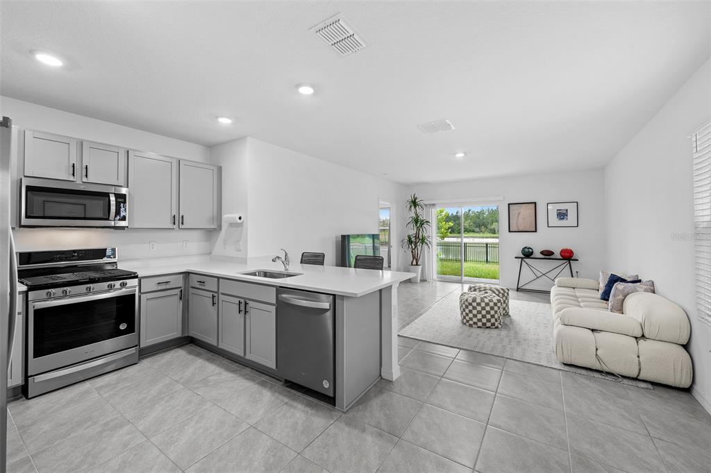 A modern kitchen with gray cabinets and white countertops opens into a bright living area — 35630 KINSEY POINT, ZEPHYRHILLS, FL