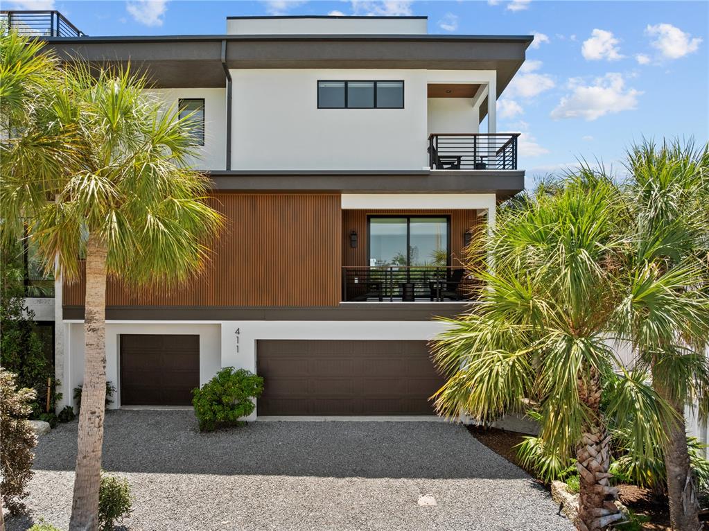 A modern three-story house features a gravel driveway, two garage doors, and wood-slat siding — 411 PALM AVENUE, ANNA MARIA, FL