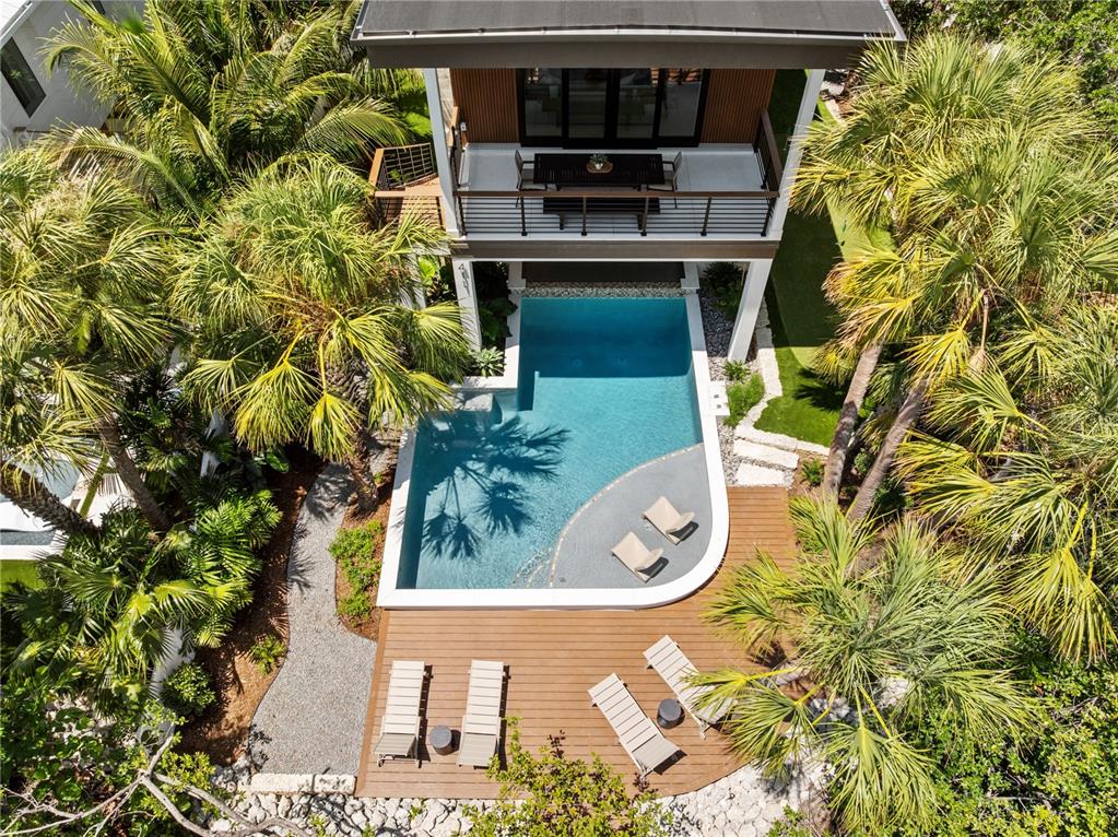An aerial view shows a modern house with a balcony, swimming pool, and wooden deck — 411 PALM AVENUE, ANNA MARIA, FL