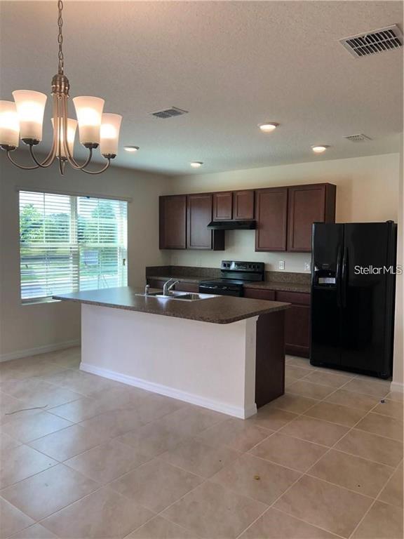 A kitchen features dark wood cabinets, a central island, and a black refrigerator — 1851 RED CANYON DRIVE, KISSIMMEE, FL
