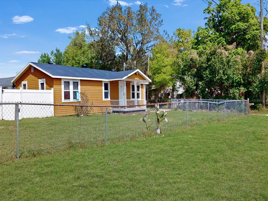 A yellow house with a dark roof sits behind a chain-link fence in a yard — 2017 MILLER BOULEVARD, FRUITLAND PARK, FL
