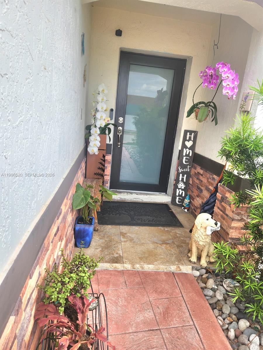 An entryway features a glass-paneled front door, stone-tiled flooring, potted plants, and a decorative sign — 14330 SW 179th Ln, Miami FL 33177, MIAMI, FL