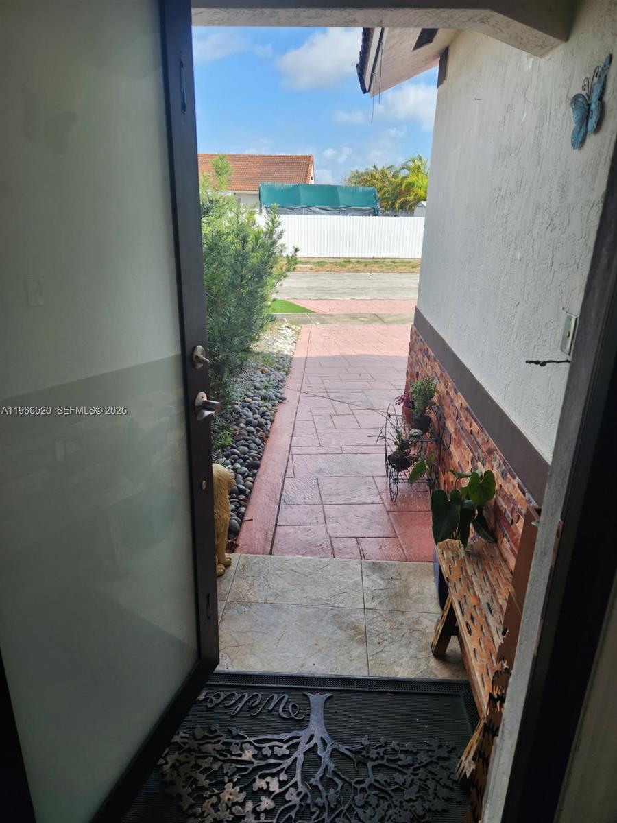 A view from an open doorway looking out onto a paved walkway and yard — 14330 SW 179th Ln, Miami FL 33177, MIAMI, FL