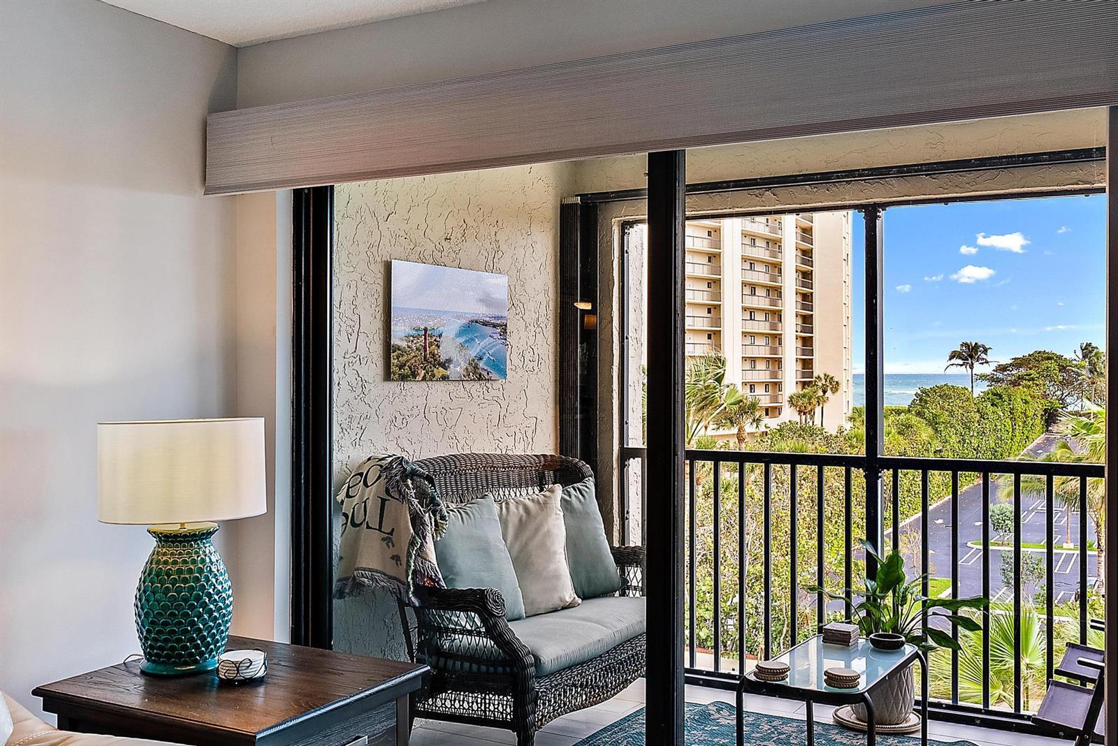 A living room opens to a balcony with wicker seating, a glass table, and ocean views — 500 Ocean Trail Way # 406, Jupiter FL 33477, JUPITER, FL