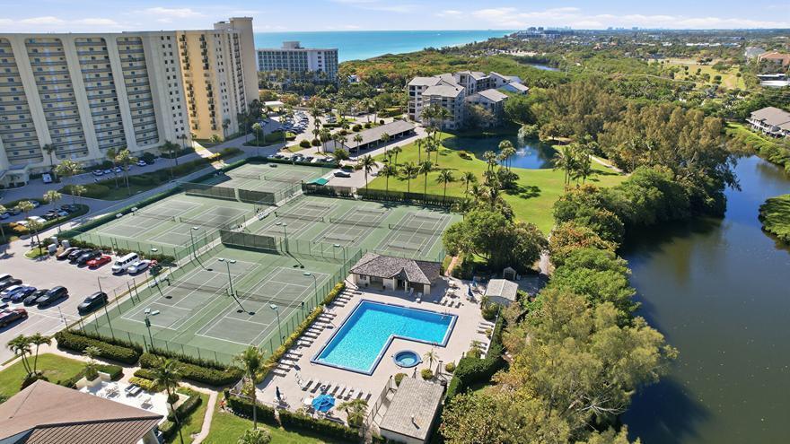 An aerial view shows tennis courts, a swimming pool, and a lake near tall buildings — 500 Ocean Trail Way # 406, Jupiter FL 33477, JUPITER, FL