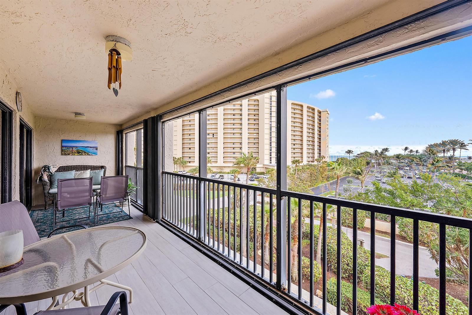 A screened-in balcony features outdoor furniture, a glass-topped table, and views of a neighboring building — 500 Ocean Trail Way # 406, Jupiter FL 33477, JUPITER, FL